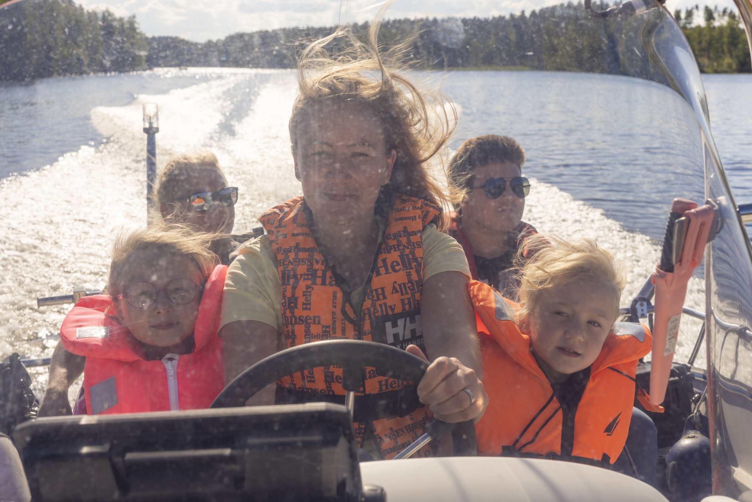 Nainen ajaa veneellä. Kyydissä kaksi lasta ja kaksi miestä.